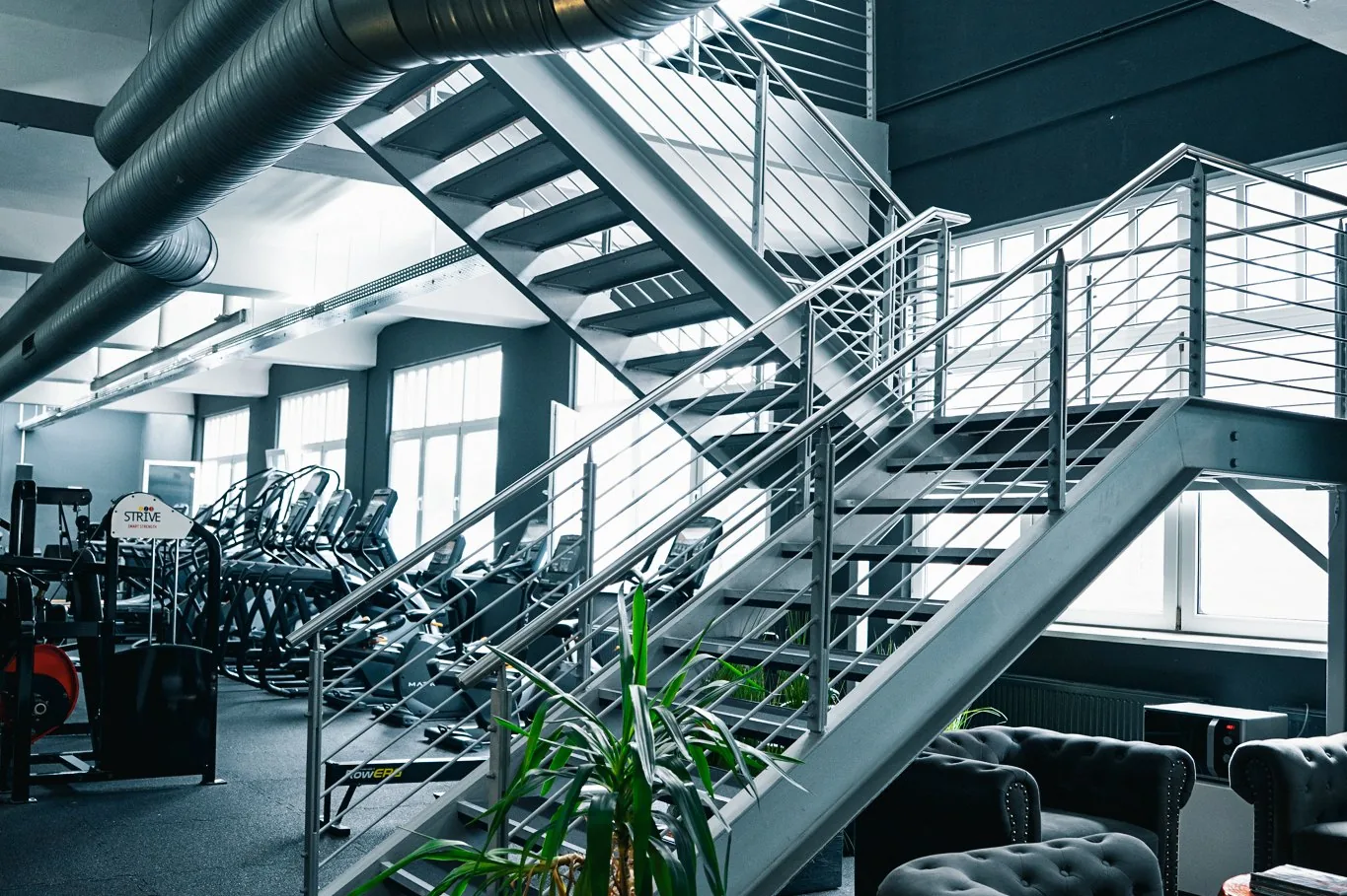 Aufenthaltsbereich mit Loungesesseln und Treppe zur Cardiofläche im Invictus Gym Hamburg