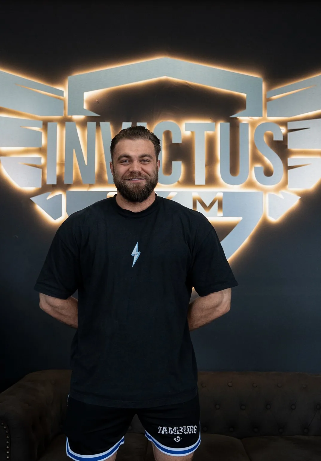 Kenneth, Studioleiter des Invictus Gym Hamburg, vor der beleuchteten Invictus-Gym-Wandlogo
